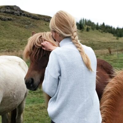 A woman with a braid lovingly caresses horses in a lush rural meadow.