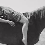 Black and white image of a person lying on a horse outdoors, exuding tranquility.