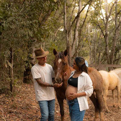 Pregnant couple enjoying a moment with a horse in a forest setting.