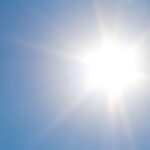 A clear blue sky with fluffy clouds and bright sunshine, representing a perfect summer day.