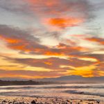 A stunning coastal sunrise with vivid clouds over a tranquil beach and sea.
