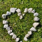 Heart-shaped stone arrangement on green grass in daylight, symbolizing nature and love.