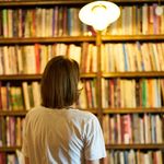Woman in a library looking at bookshelves, creating a warm and cozy atmosphere.
